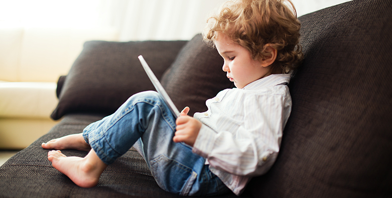 skärmtid- barn som sitter med ipad i soffan